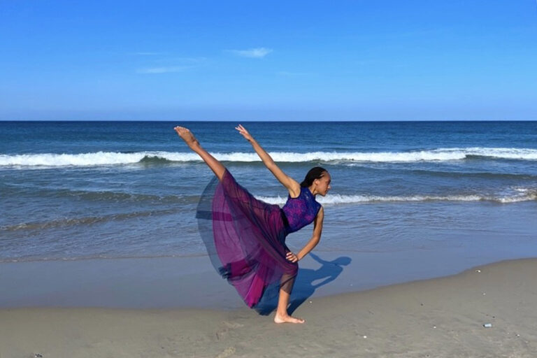 Conservation Nation Youth Advisor in a pink and purple dress and with her hair in braids poses in arabesque on the beach