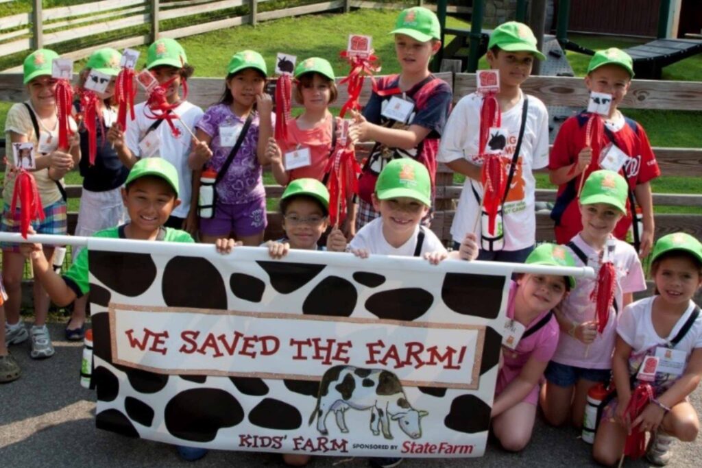 group of kids holding up a sign that reads we saved the farm, kids' farm sponsored by state farm