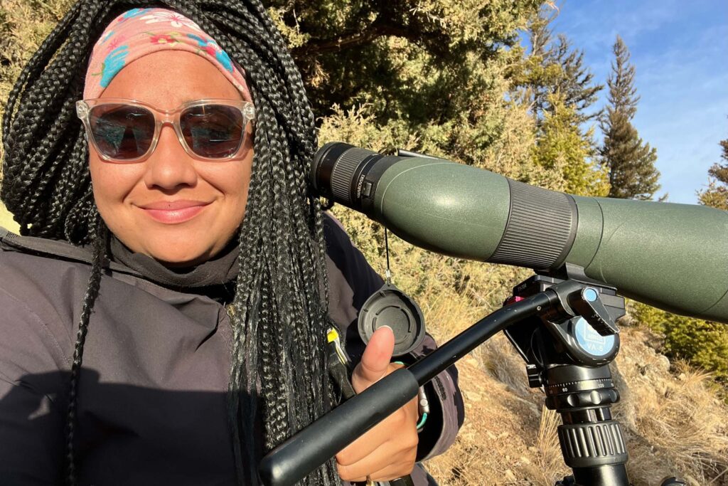 a Black woman with braided hair next to a spotting scope