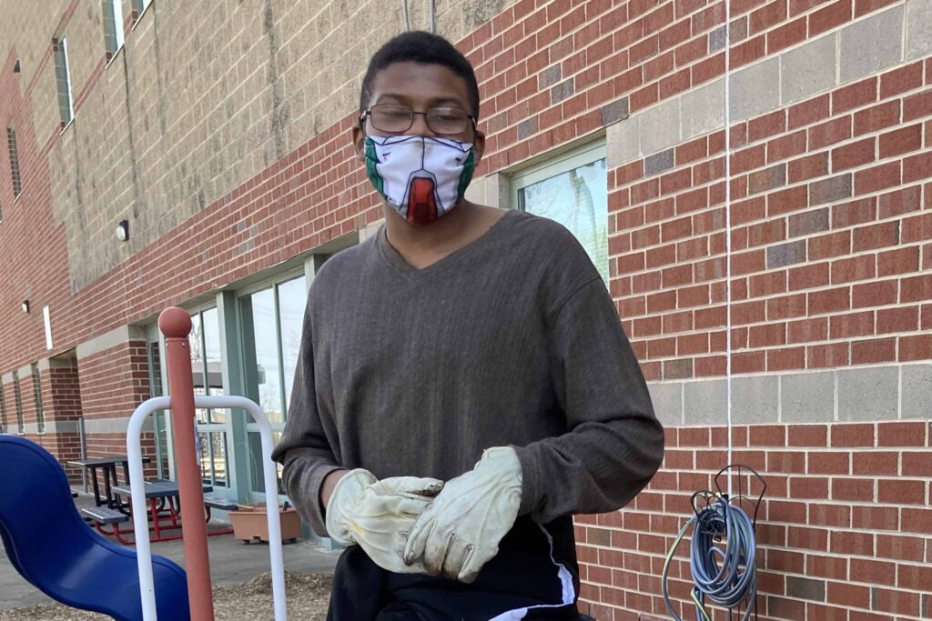 Conservation Nation's Tyler Kirkland in front of a school wearing gardening gloves