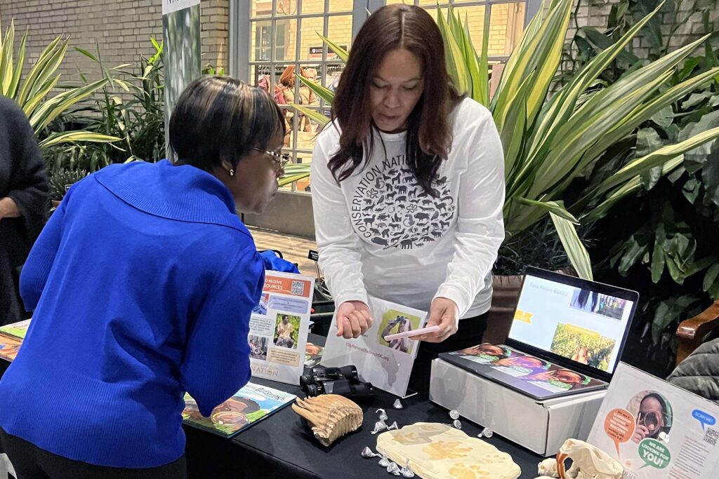 two Black women looking at a phone while standing at a table filled with educational material