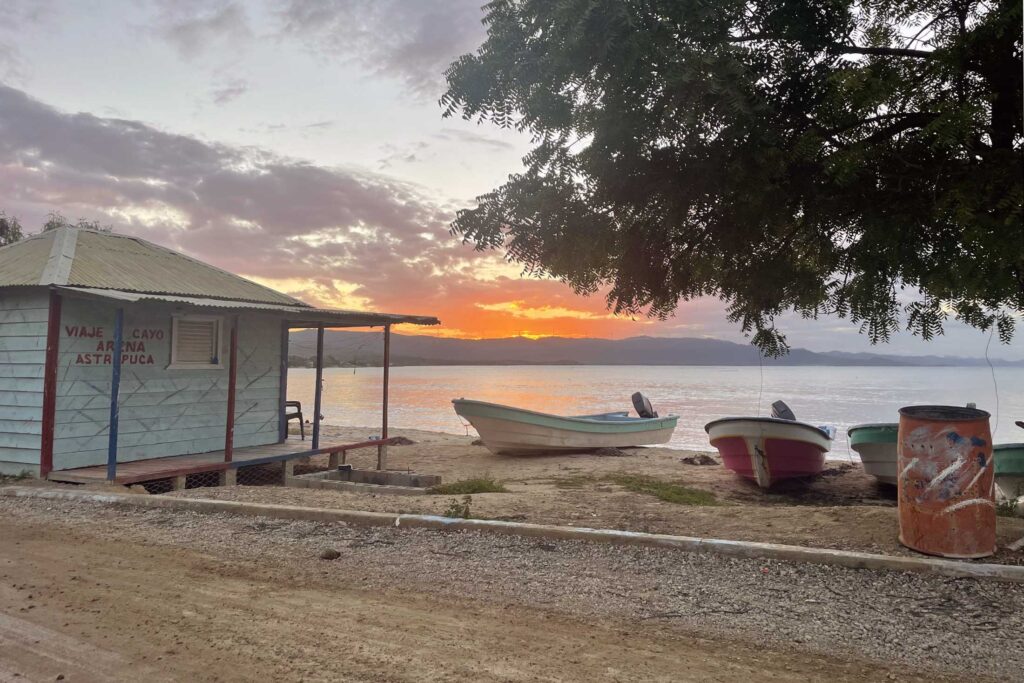 sunset over the water with boats and a small building in the foreground