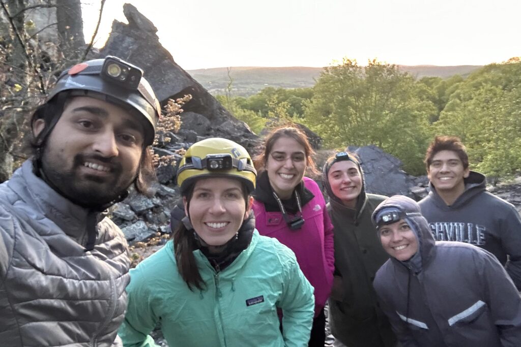 six young adults wearing hiking gear and posing for a photo with rocks and trees in the background