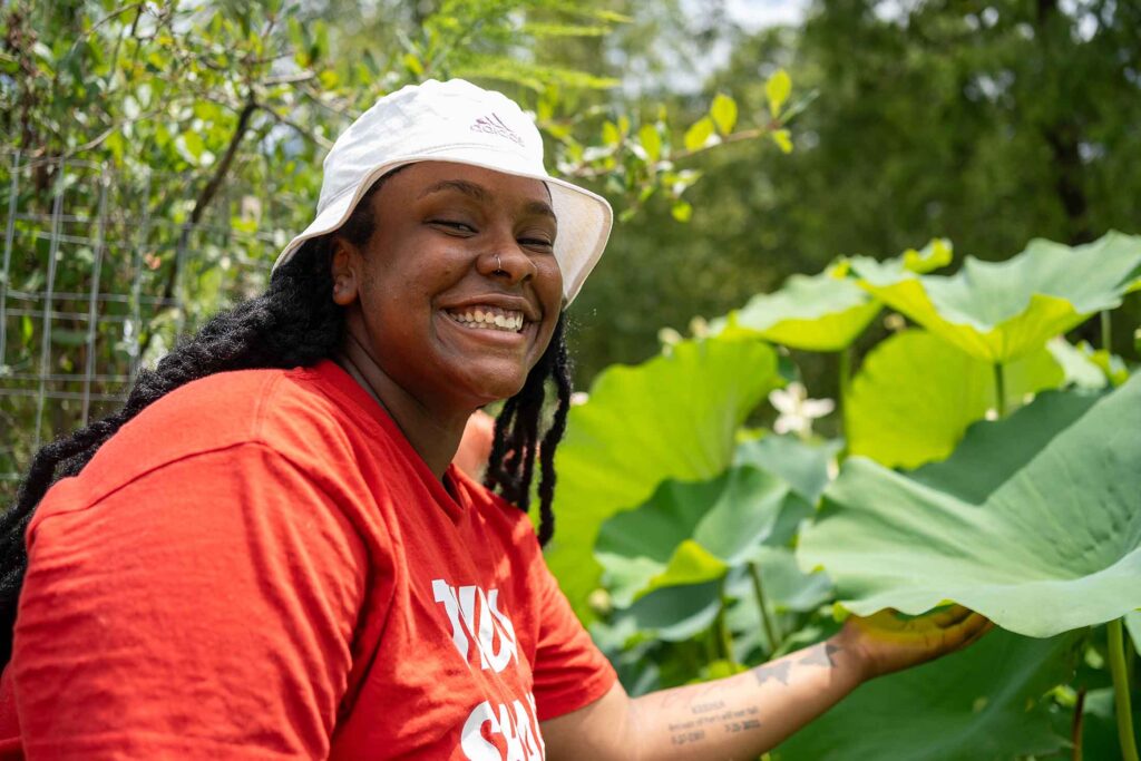 a young Black woman wearing a red shirt and putting her had under a large green leaf