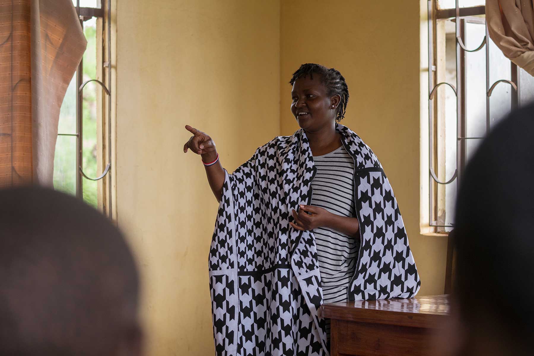 a black woman wearing black and white patterned clothing speaking to other people in a room