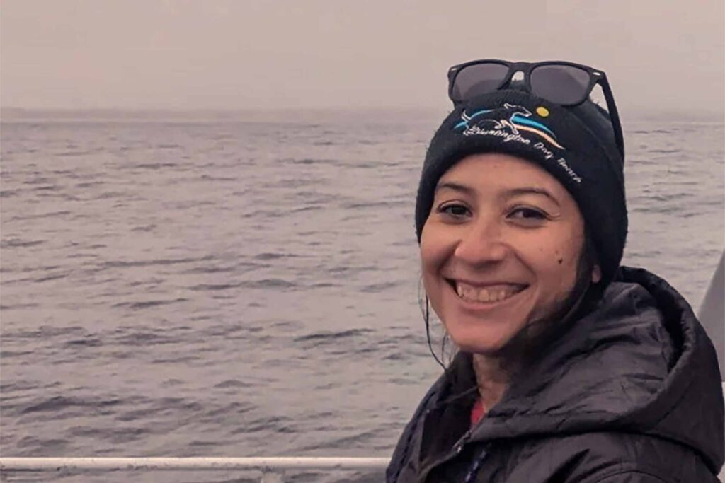 a woman wearing a hat and coat with sunglasses on her head on a boat with water and gray skies in the background