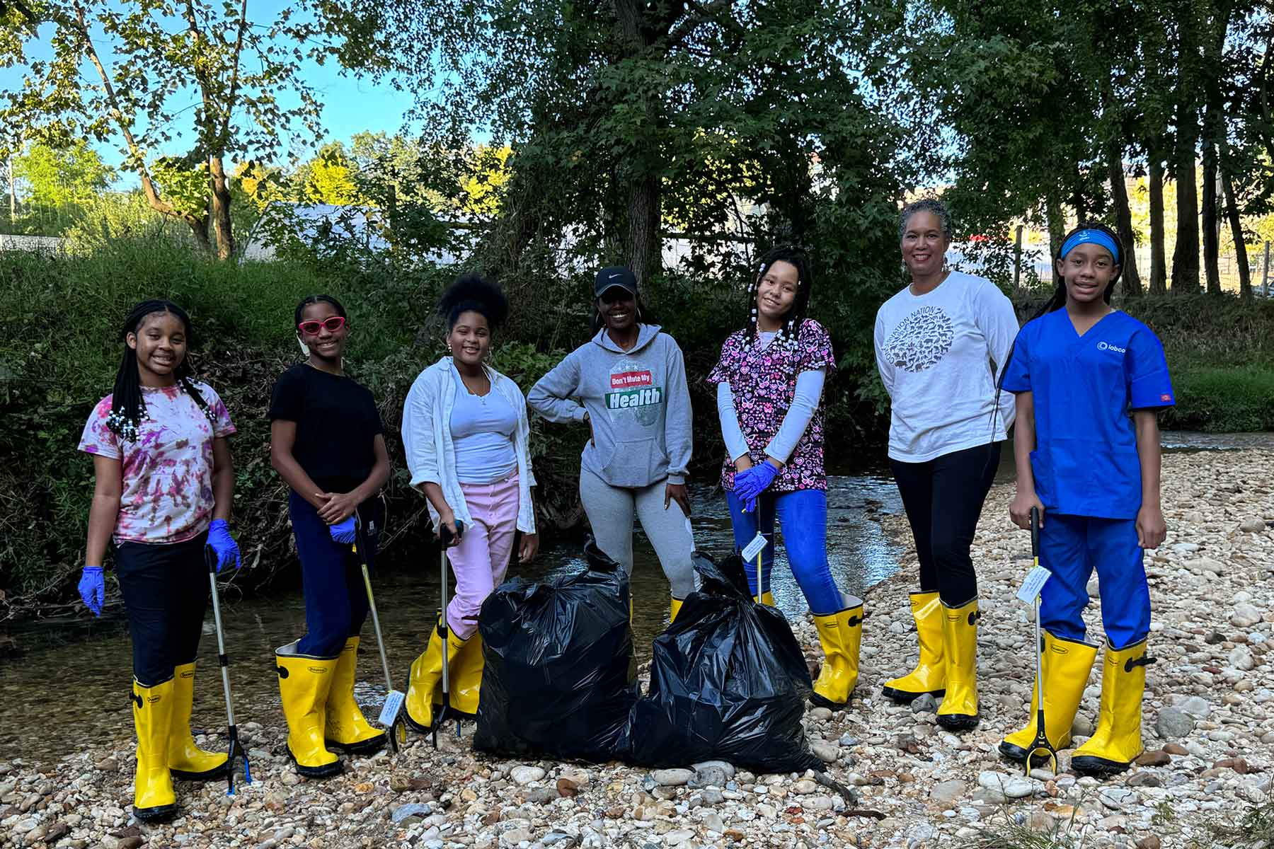 a group of young Black women wearing yellow rian boots and standing by a stream