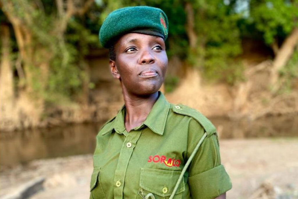 a Black woman in Africa wearing a green beret and green shirt with a logo with trees in the background