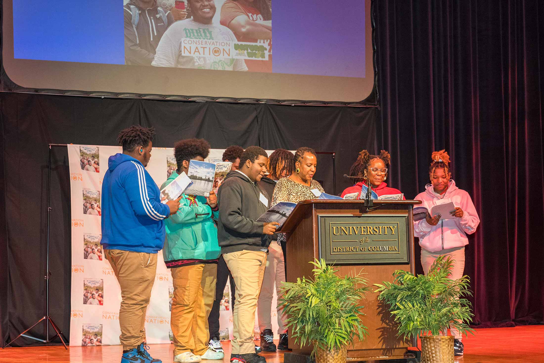 a group of people on stage reading from a book in front of a podium with as sign that reads university of the district of columbia