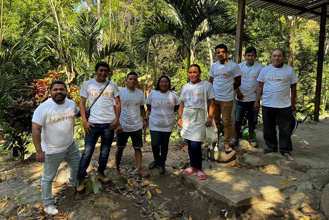 a group of people standing under a covered structure in a wooded area in the jungle wearing t-shirts that read conservation nation