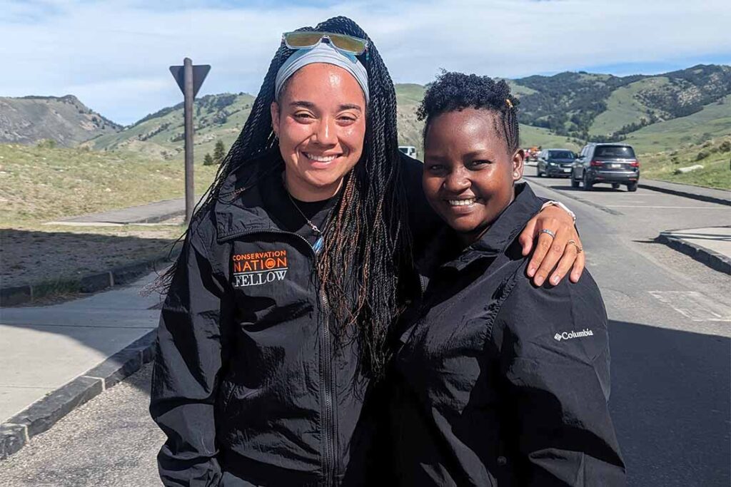 two Black women wearing black coats smile for the camera