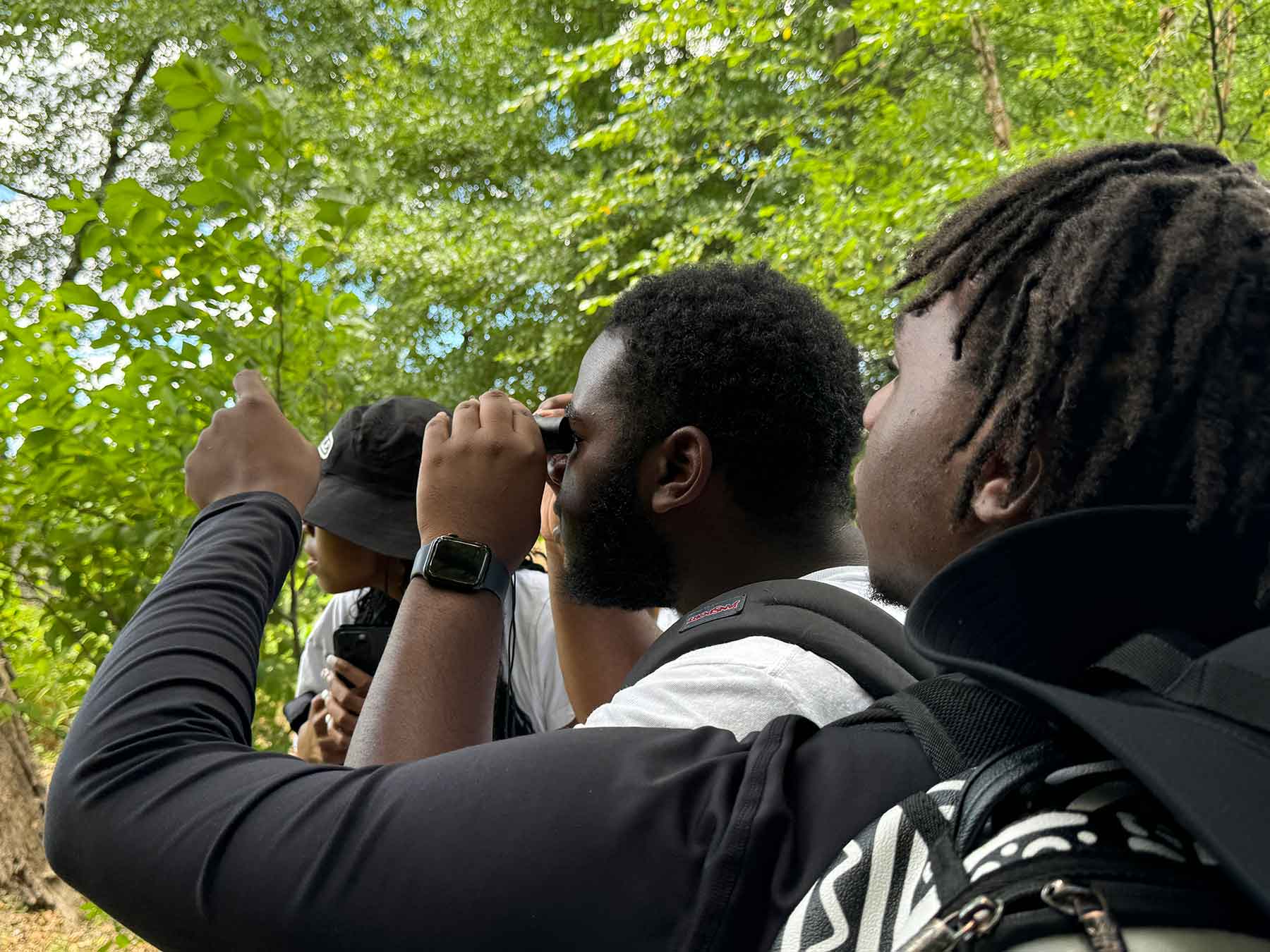 two young Black students use binoculars to observe something in the woods