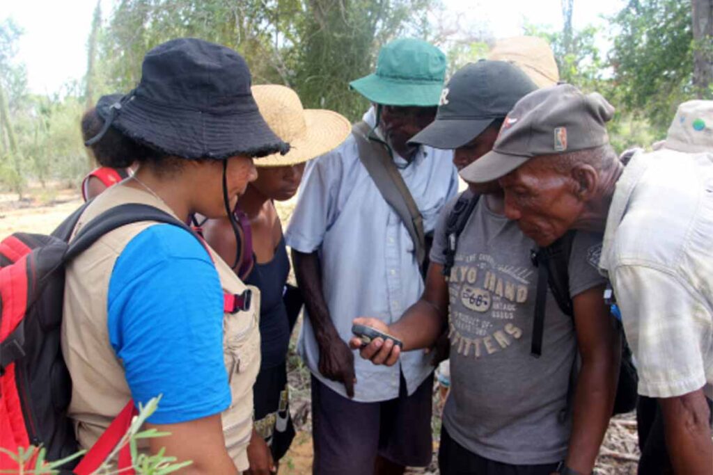 a small group of adults wearing hats looking at a portable device that one of them is holding