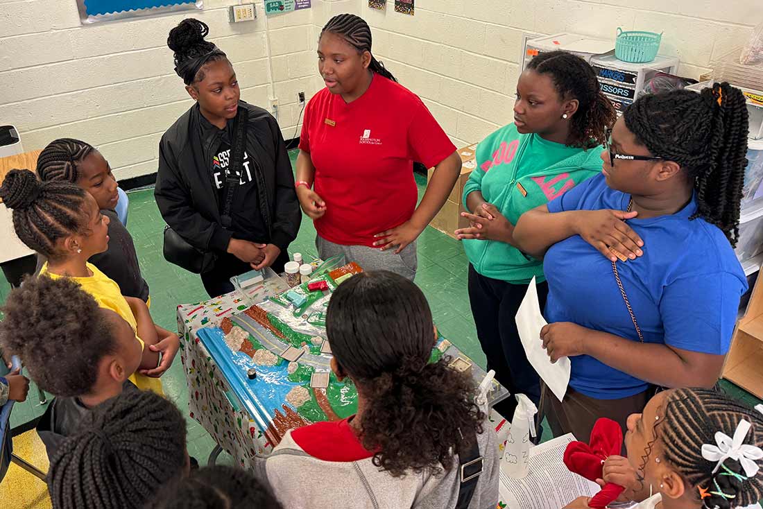 A group of Black students wearing colorful clothing standing around a table