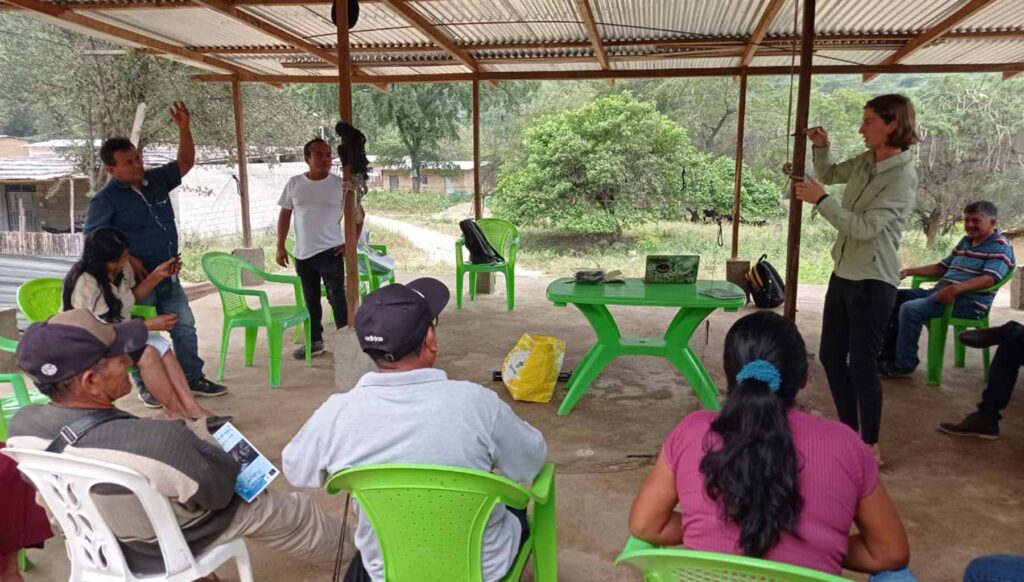 a female scientist demonstrating how to use equipment to a group of people sitting and standing beneath a canopy