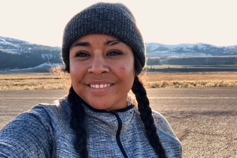 a woman wearing a beanie hat taking a selfie with mountains in the background