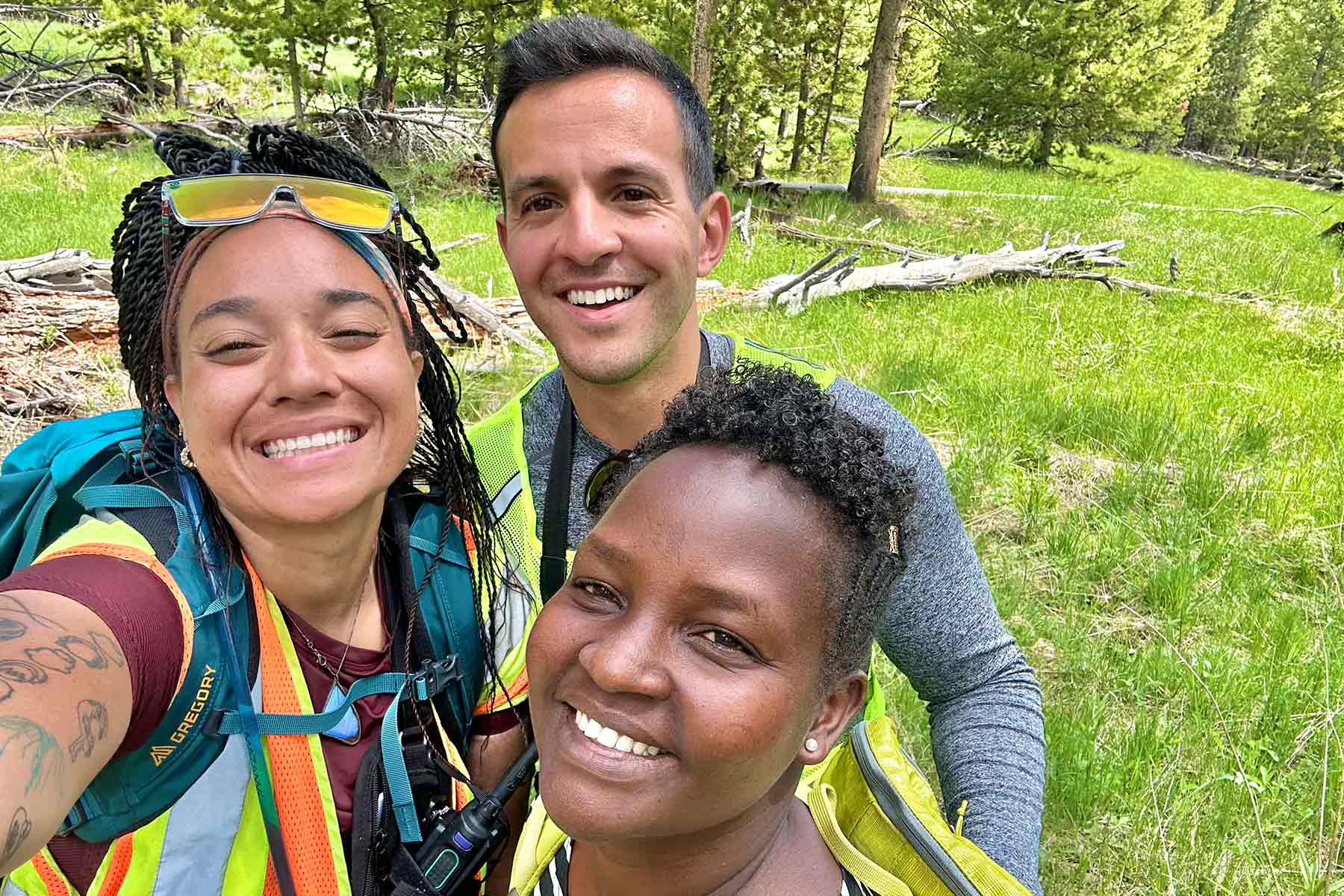 three young adults taking a selfie while standing in a clearing near a wooded area