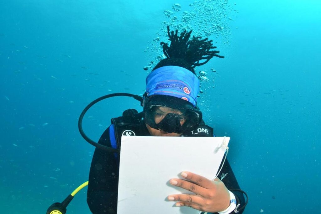 a brown-skinned woman with black hair taking notes under water while scuba diving