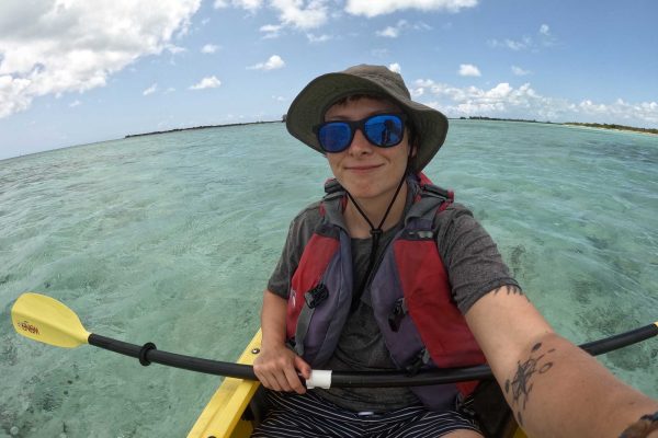 a kayaker wearing a hat and sunglasses taking a selfie with clear water in the background