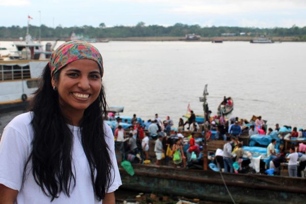 a woman wearing a bandana in a fishing village with local people on a boat in the background
