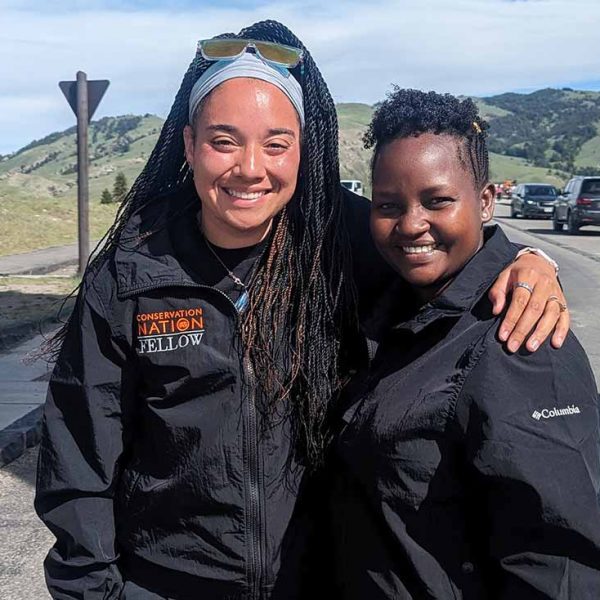 two Black women wearing black coats smile for the camera